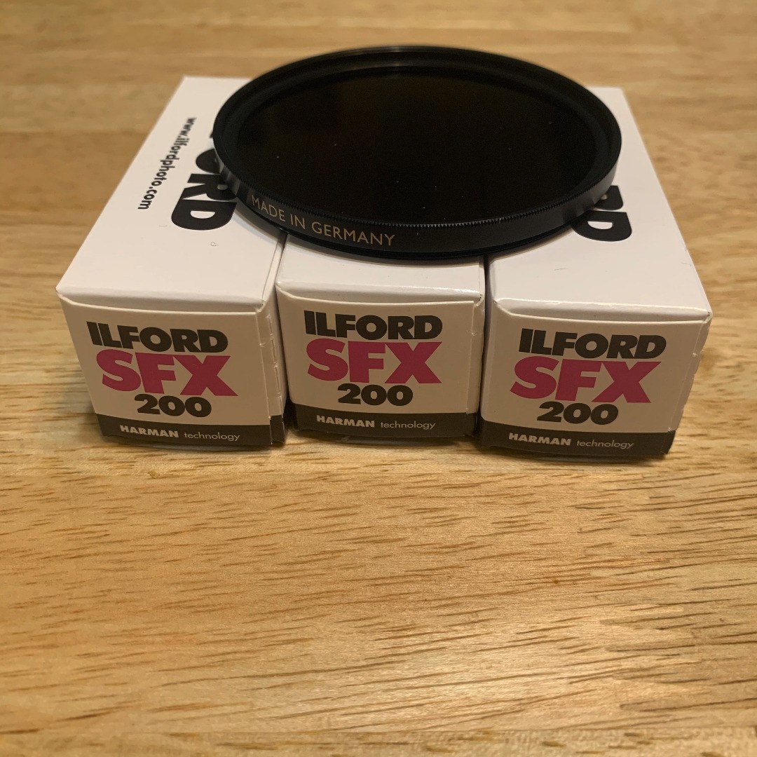Photo of three 120 film rolls in boxes that say "Ilford SFX 200 Harman Technology" on them with a large, dark filter on top