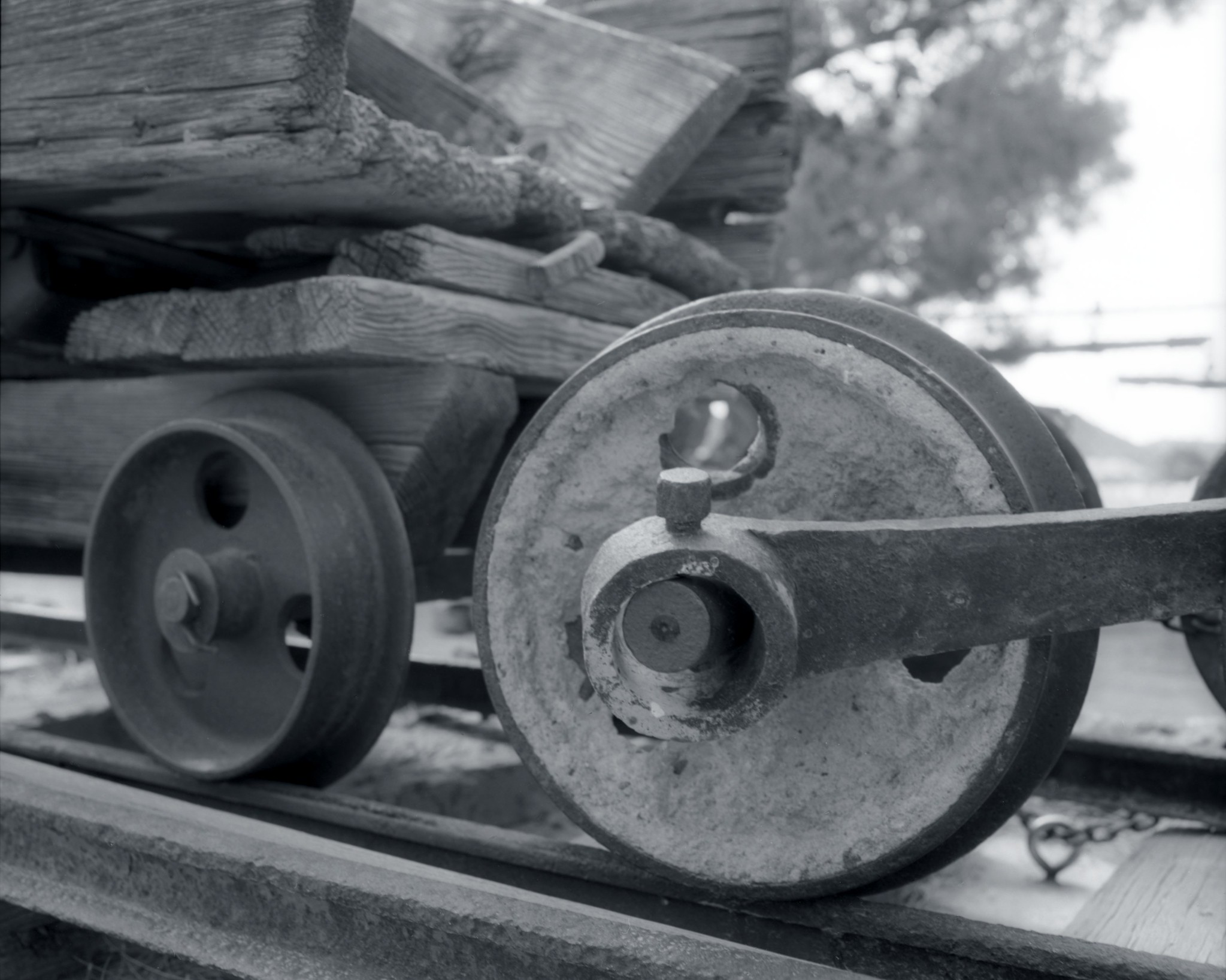 Black and white photo of the front of an antique mine cart, with the wheel large and close up in the bottom right of the photo.