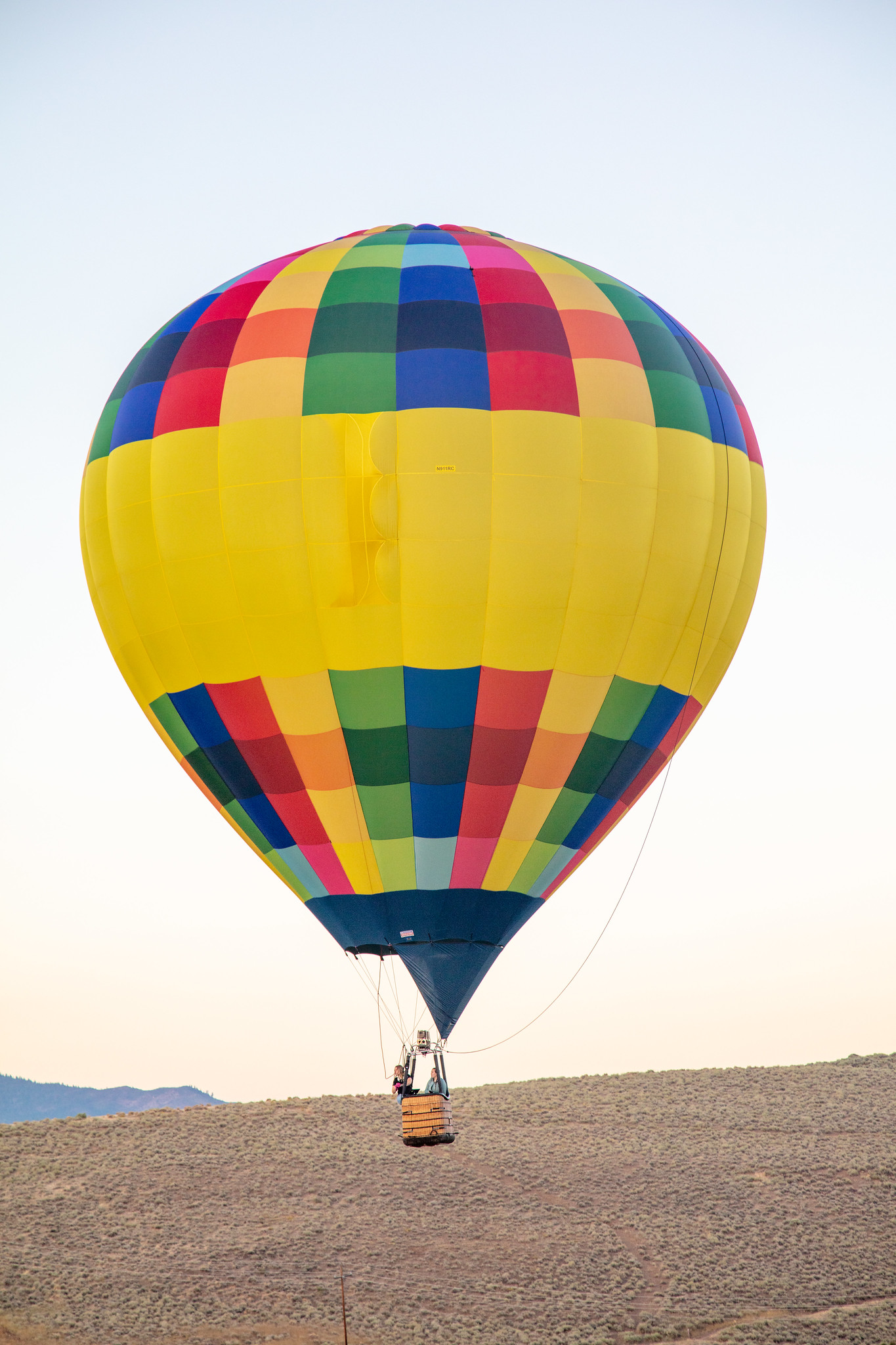 Photo of hot air balloon piloted by two people, hovering above an arid plain