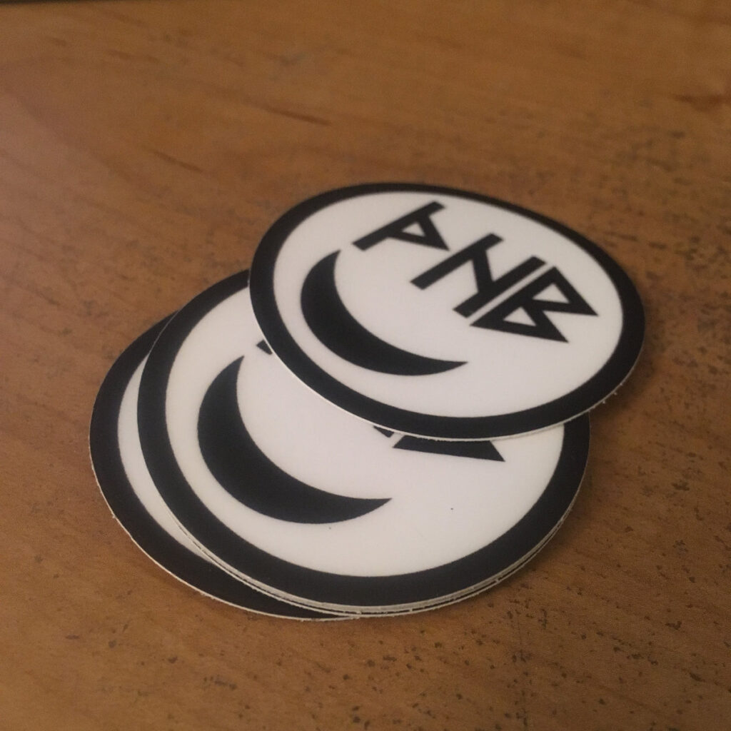 Photo of pile of circular stickers with white background and face made of a moon and the runes representing The Happy Buttons